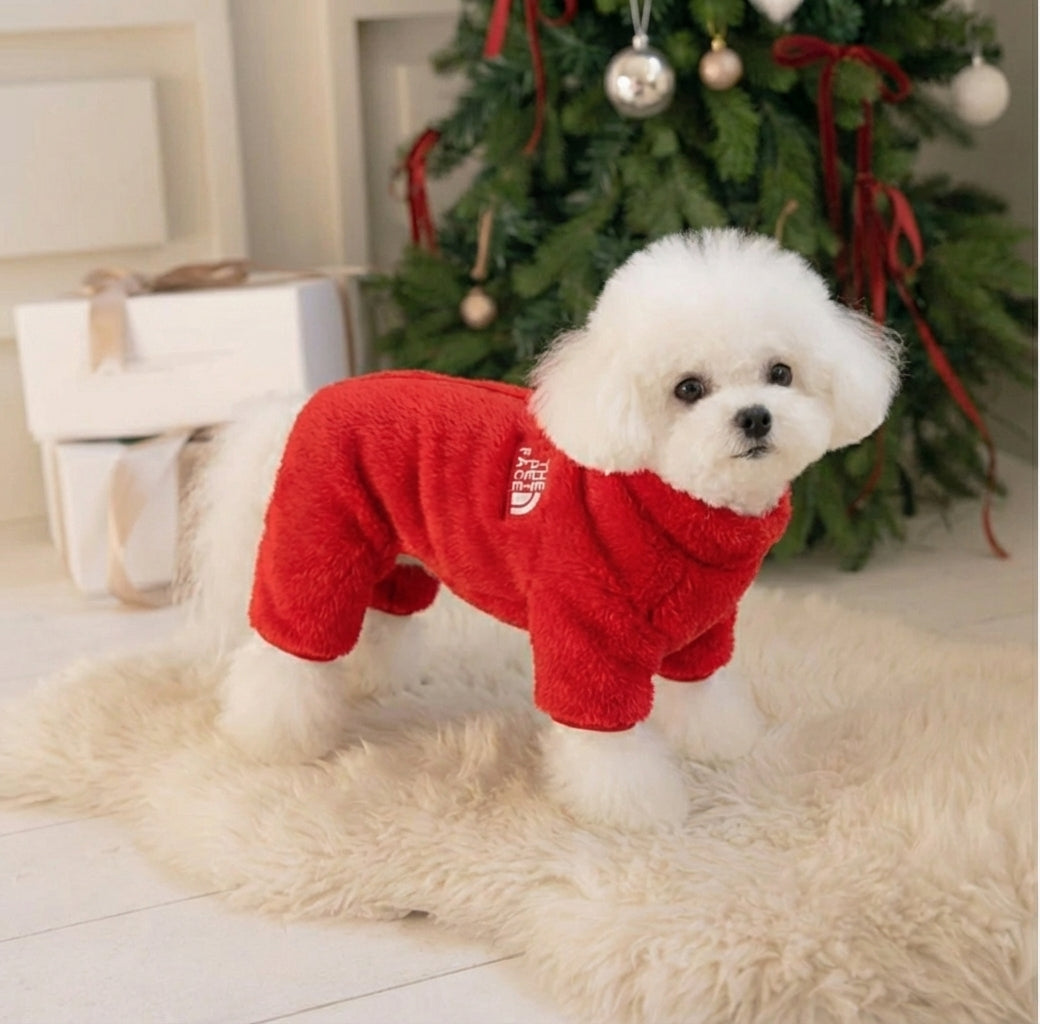 赤色の犬用フリースジャンプスーツ（Petopop製）、クリスマスツリーとプレゼントの近くにある白い毛皮の敷物の上