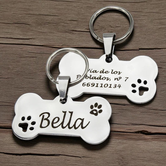 Stainless steel bone-shaped pet ID tags with engraved names and paw prints by Petopop, displayed on wooden surface